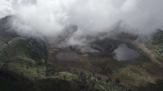 Aerial Cinematic View of Misty Volcanic Highlands with Reflection Lakes and Rolling Clouds at Kawah Bulan Sabit, Banyuwangi, East Java, Indonesia.