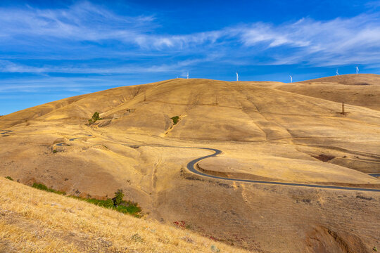 A winding country road surrounded by desert hills and wind turbines