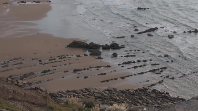 Ocean waves washing over rugged intertidal rock formations, creating lines and patterns along the exposed flysch coast