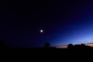 Moon on a twilight sky with stars, planets and landscape mountain silhouettes. © astrosystem
