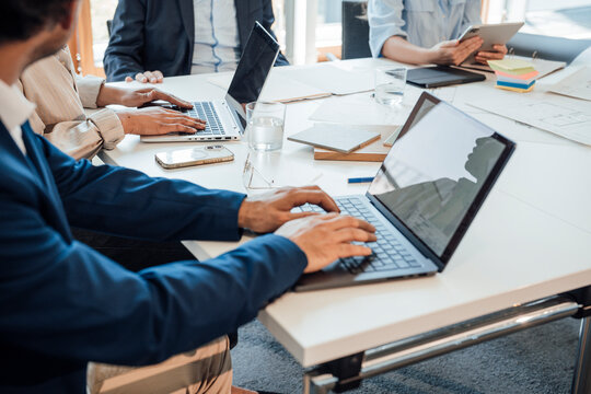 Business colleagues type on laptops during an office meeting