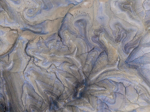 Aerial view of the rugged, eroded desert landscape with intricate patterns of sedimentary rock formations, deep gullies, and textured earth in Hanksville, Utah, United States.