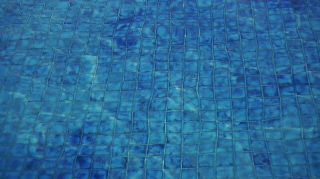 Clear blue swimming pool water texture with ceramic tile pattern visible beneath the calm surface.	