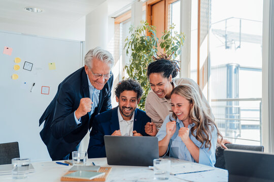 Business team celebrates success looking at laptop in the office