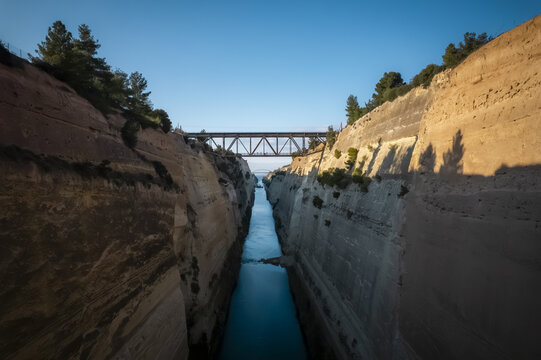 Aerial view of the Corinth Canal with steep limestone walls and a metal bridge spanning the narrow waterway in Archea Korinthos, Greece.
