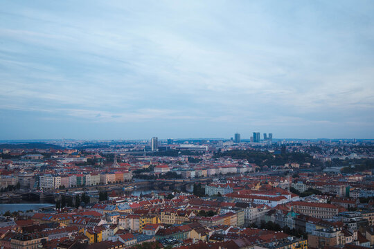 Aerial view of the historic city of Prague with its iconic red rooftops, bridges spanning the Vltava river, and modern skyline under a soft evening sky in Prague, Prague, Czechia.
