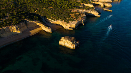 Fototapeta premium Picturesque coastal landscape of rugged limestone cliffs and clear turquoise water. Rocky cape over sea bay with stony shore under sunlight. Algarve, Portugal