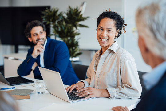 Smiling businesswoman types on laptop during office meeting