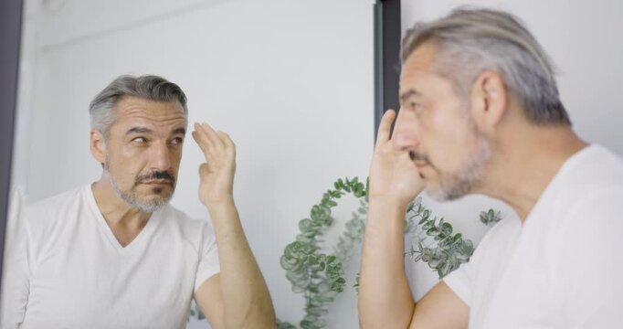 Senior caucasian man at mirror makeup routine with copy space. Beauty influencer guy with perfect skin dress up. Healthcare man lifestyle cosmetic blogger