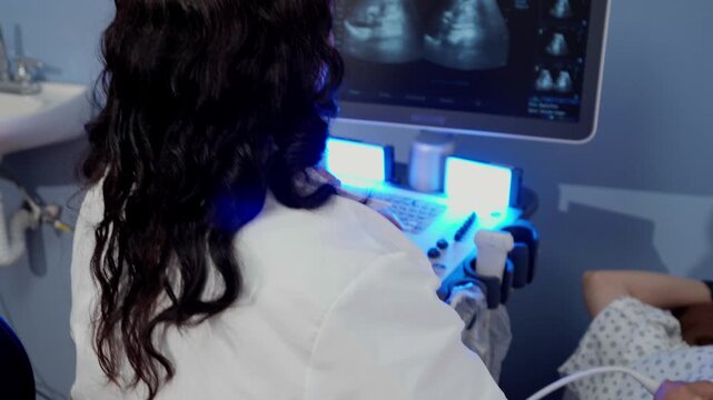 Panning shot of a female doctor performing an abdominal ultrasound on a young Latina woman lying on an examination table in a modern medical clinic with blue LED lighting.