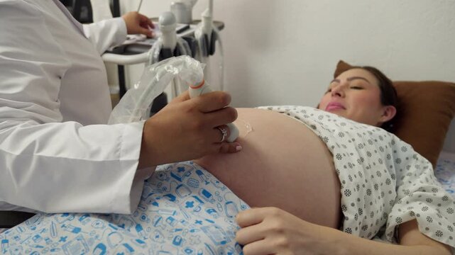 A doctor performs a routine prenatal ultrasound on a calm nine-month pregnant Mexican woman in a clinic, applying gel and moving the transducer across her abdomen.