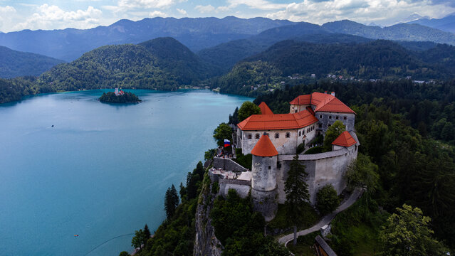 Aerial view of Bled Castle perched on a cliff overlooking the turquoise waters of Lake Bled with the Julian Alps in the background in Bled, Radovljica, Slovenia.