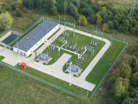 Aerial view of 110kV substation with electrical transformers and a white utility building surrounded by a fenced perimeter and lush green vegetation in Krakow, Lesser Poland Voivode, Poland.