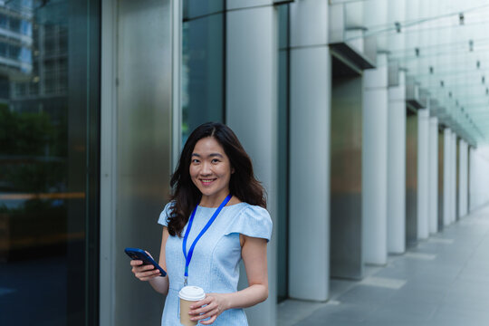 Smiling businesswoman holds a smartphone and coffee outdoors