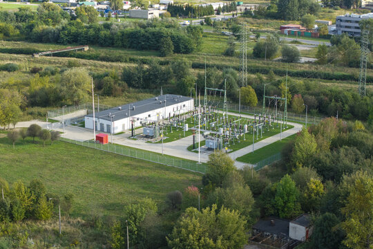 Aerial view of 110kv substation with electrical equipment, transformers, and metal structures, surrounded by green fields and trees in Krakow, Lesser Poland Voivode, Poland.