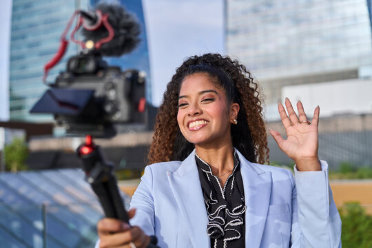 A smiling businesswoman waves and films a video in the city