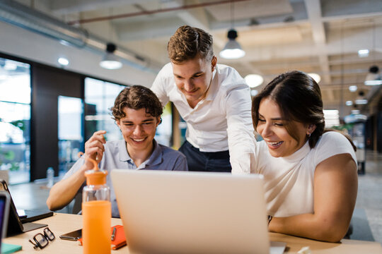 Smiling coworkers collaborate on a laptop in an office