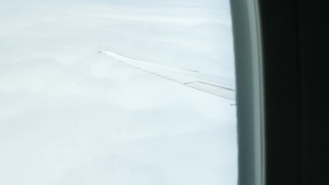 Aerial view through plane window with view of airplane wing over puffy white cloud with clear blue sky while flying, View from the window of the plane traveling by air, vacation background concept