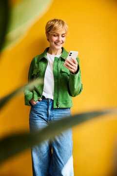 Smiling woman uses smartphone against yellow wall