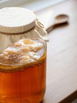 Kombucha fermenting tea drink with scoby in glass jar on a wooden surface with a blurred wooden spoon, healthy gut and probiotic beverage concept