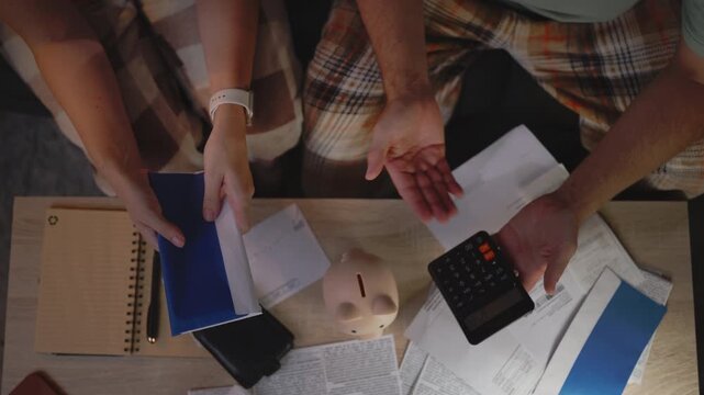 Concerned couple sitting together at home and reviewing unpaid bills, calculating available money and struggling to cover household expenses while facing financial difficulties.