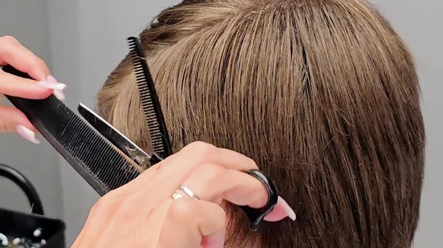 Barber cutting a teenager's hair in a barbershop, using scissors and comb during a professional haircut, with salon tools and equipment clearly visible in the background in the salon setting