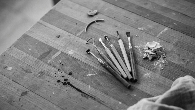 Collection of metal sculpting implements on a worn wooden table with sculpting modeling workshop instrument equipment creative monochrome overhead hardwood technical close-up implement