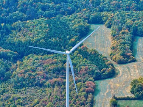 Aerial view of the Parc eolien des trois cantons wind turbine rising above the dense autumn forest and agricultural fields in Etouvans, Bourgogne-Franche-Comte, France.