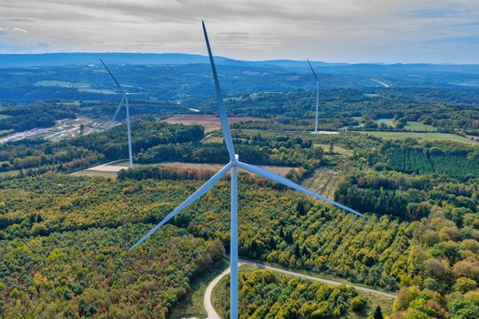 Aerial view of the Parc eolien des trois cantons wind farm with large wind turbines rising above a dense forest and rolling hills in Etouvans, Bourgogne-Franche-Comte, France.