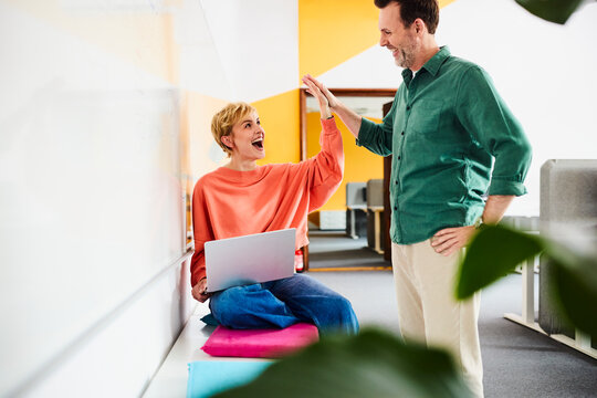 A man and woman celebrate success with a high five in the office