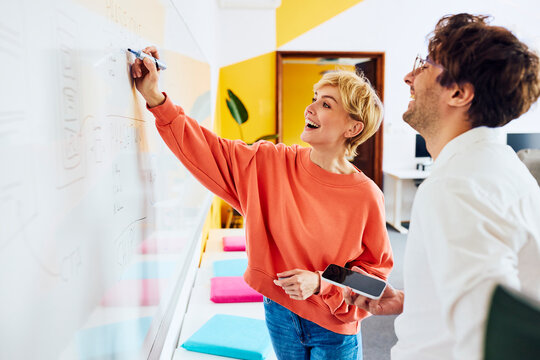 Smiling colleagues brainstorm on a whiteboard in the office