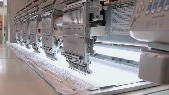 Row of Embroidery Heads Working Over a Long Fabric Surface. The footage documents textile equipment, material handling, stitching or machine controls in a workshop.