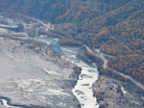 Aerial view of Knik River winding through a vast landscape with autumn-colored forests, gravel riverbeds, and sparse evergreen trees in Knik River, Alaska, United States.