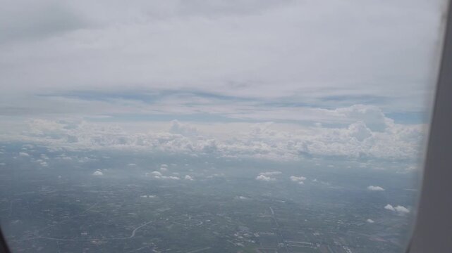 aerial footage view flying in the sky with some clouds over green landscape through airplane window. aerial view of cloud in sky in natural nature background flying in the sky above countryside area