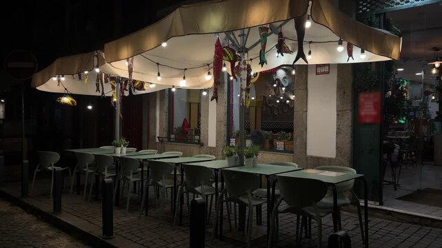 Outdoor cafe terrace at night, empty tables and chairs under warm lights