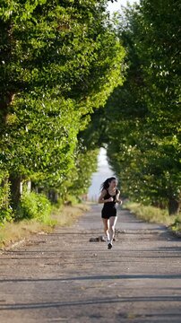 Young Athletic Woman In A Black Sport Suit, Runs Along The Road In A Park