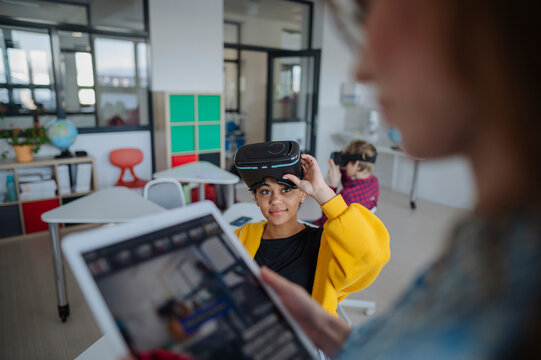 Teacher guiding teenage student using virtual reality technology at school.