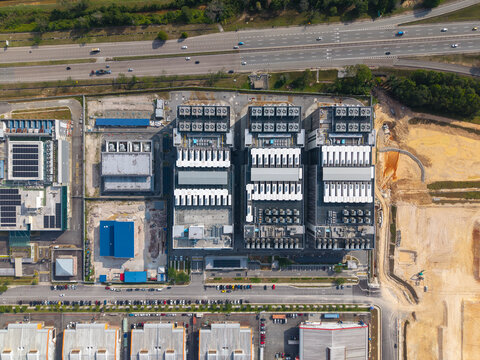 Aerial view of a modern data center facility with large industrial buildings and rooftop cooling systems, adjacent to a highway and parking area in Iskandar Puteri, Johor Darul Ta'zim, Malaysia.