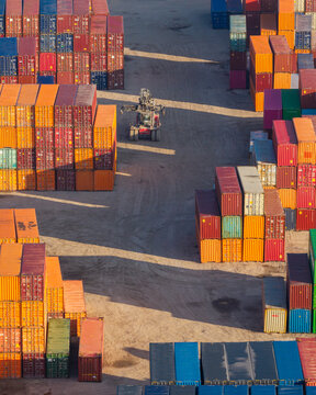 Aerial view of a busy shipping container terminal with stacks of colorful containers and a reach stacker vehicle operating in the industrial port area of Warszawa, Mazowieckie, Poland.