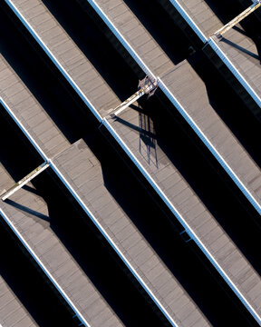 Aerial view of a warehouse roof with repeating parallel structures and long shadows in Warsaw, Mazowieckie, Poland.