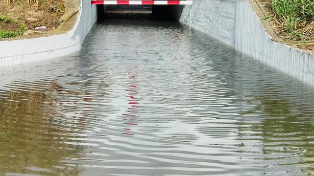Flooded underpass tunnel with rippling water and red and white barrier after rain
