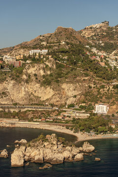 Aerial view of Isola Bella, a small island connected to the beach by a thin strip of sand, with rocky cliffs and the town of Taormina on the hillside in Taormina, Sicily, Italy.