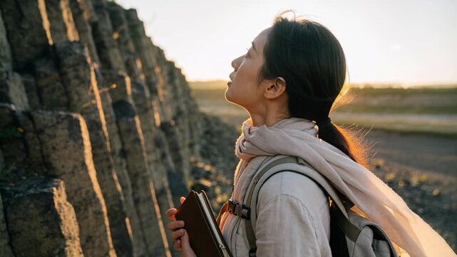 Walking woman studying basalt columns at coast for study, holding brown notebook, scarf, copy space