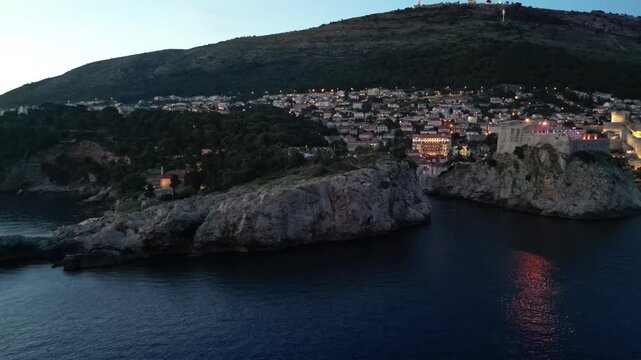 Illuminated Fort Lovrijenac And The Rocky Dubrovnik Coastline At Dusk With City Lights Below Mount Srd In Croatia. - aerial shot