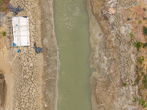 Aerial view of a shrinking river with dry, cracked mud banks during the dry season in Kedung, Central Java, Indonesia.