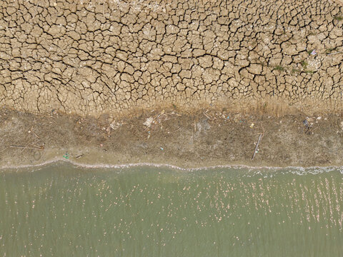 Aerial view of a shrinking river with dry, cracked mud banks and scattered debris during the dry season in Kedung, Central Java, Indonesia.