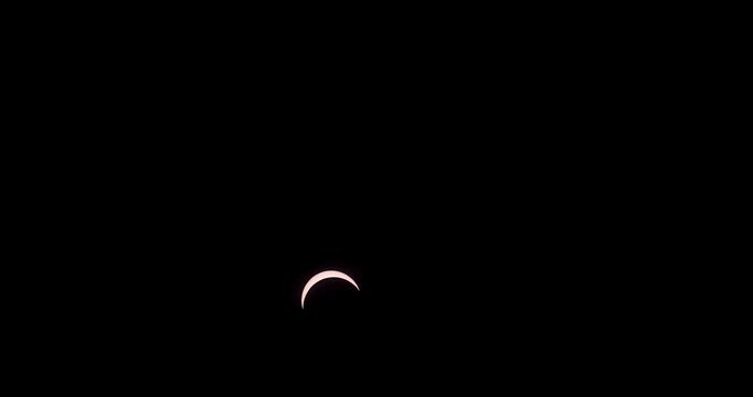 A partial solar eclipse moves across a dark black sky, highlighting the sun and moon alignment in timelapse.