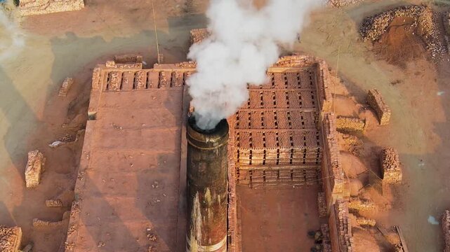 Aerial view of a brick kiln smokestack emitting white smoke over stacked bricks. Environment pollution