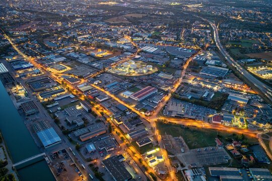 Aerial view of the industrial district of Mulhouse illuminated at night, featuring warehouses, storage tanks, and a network of roads alongside a canal in Mulhouse, Grand Est, France.