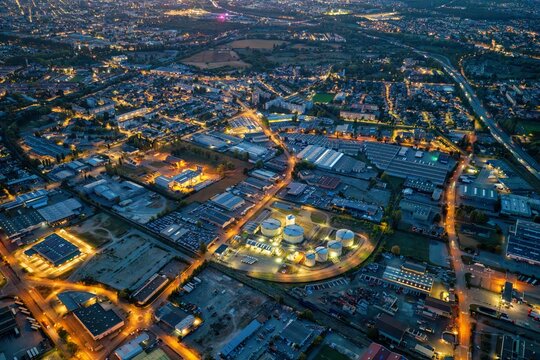 Aerial view of the illuminated industrial area and urban landscape of Mulhouse at night, featuring storage tanks and glowing street lights in Mulhouse, Grand Est, France.